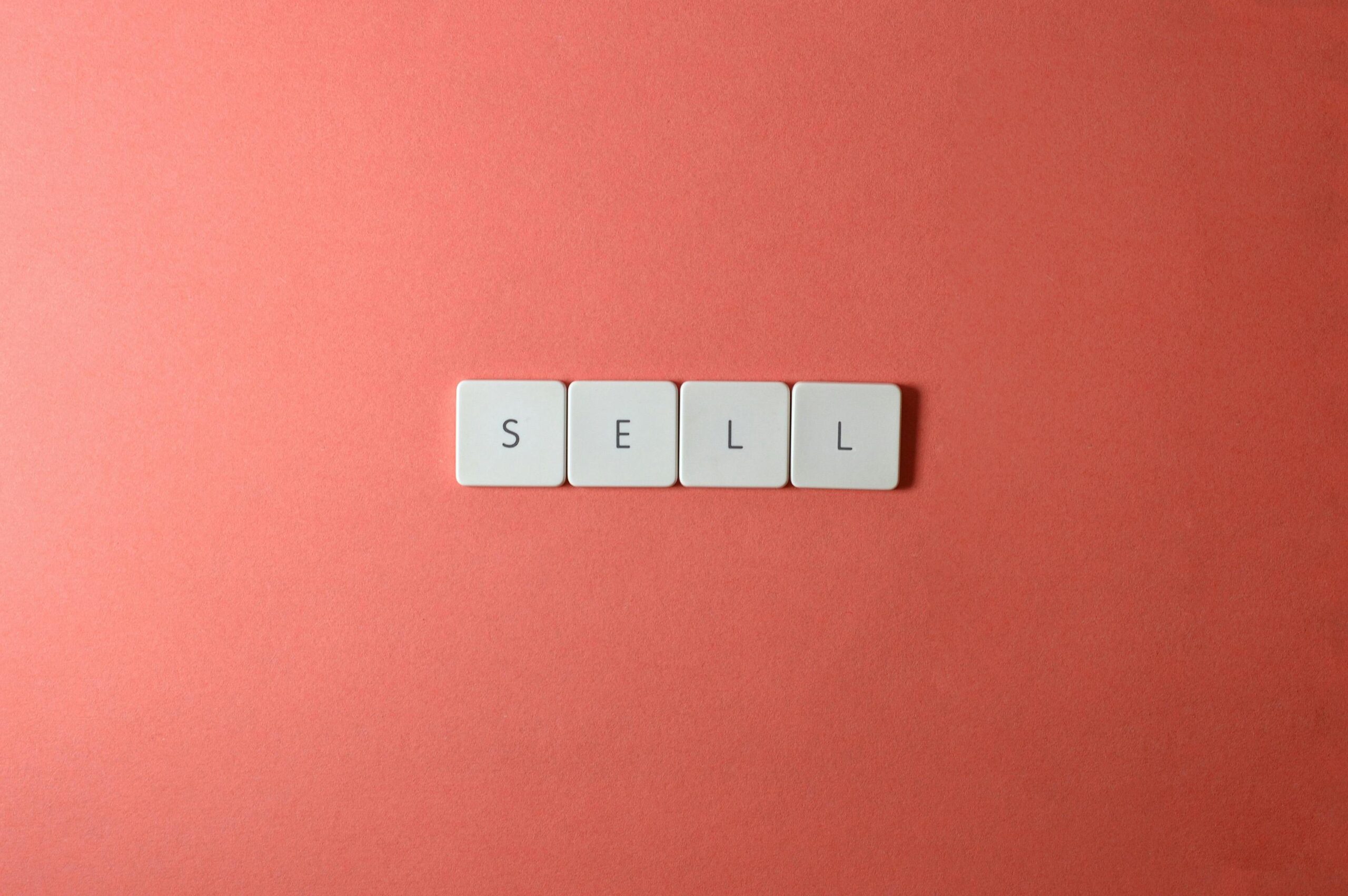 Close-up of keyboard tiles spelling 'sell' on a red background, minimalist design.